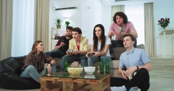 Attraktiva tre kille och tre damer har en rolig tid tillsammans hemma i vardagsrummet de spelar ett video spel två av dem någon gjorde t passera nivån och bli upprörd, de dricker lite öl från en grön — Stockvideo