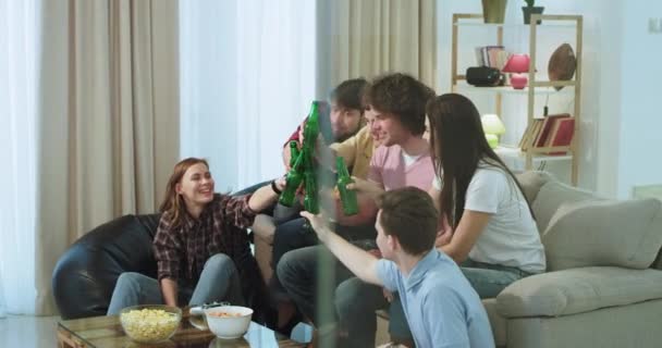 Feche um grande grupo de amigos em uma sala de estar assistindo o jogo de futebol na frente da TV muito concentrada com um rosto carismático comer pipocas e beber um pouco de cerveja — Vídeo de Stock