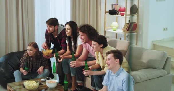 In a modern living room excited group of friends multi ethnic watching on the TV a football match they support their favorite team while drinking some beer — Stock Video