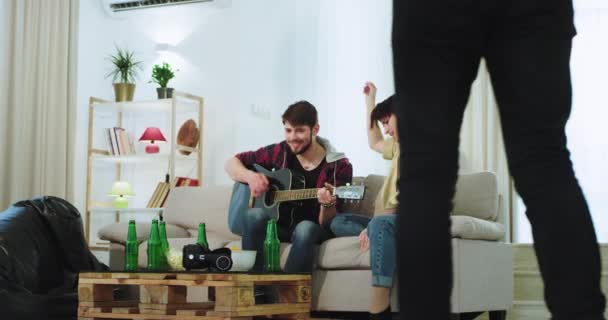 Bir arkadaş parti çok etnik arkadaşlar bir gitar üzerinde oynayan ön cadı yakın geliyor gitar gitar üzerinde gitar şarkı söyleyen bir adam ile iyi görünümlü bir bayan , geniş bir oturma odasında — Stok video