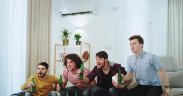 En una amplia sala de estar un grupo de amigos hombres que celebran la victoria de su equipo muy emocionados y gritando se levantan del sofá y se sienten felices — Vídeos de Stock