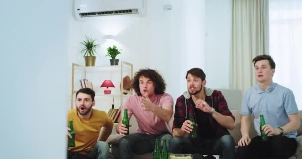 Partido de fútbol frente al televisor para una gran compañía de chicos multiétnicos que celebran el gol de su equipo de fútbol, mientras beben cerveza y se sienten emocionados. tiro en épica roja — Vídeos de Stock