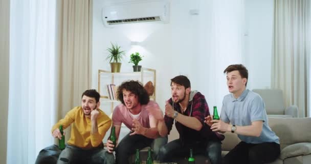 En una moderna sala de estar carismático cuatro chicos multiétnicos celebrando la victoria de su mejor equipo de fútbol viendo en el frente de la televisión — Vídeo de stock