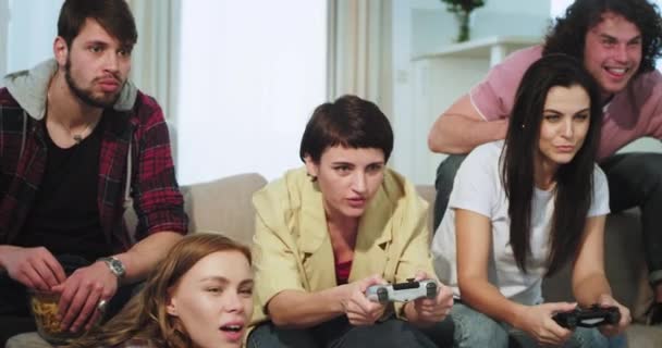 Buen grupo de amigos muy carismáticos pasar un buen rato juntos en el sofá en la sala de estar dos de las damas jugando en un juego virtual — Vídeos de Stock