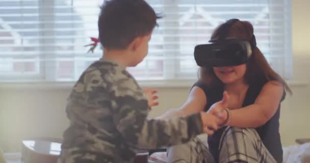 Anak laki-laki yang lucu dengan adik perempuannya bermain bersama di kamar tidur di atas tempat tidur, adik perempuan menonton sesuatu di kacamata virtual reality-nya . — Stok Video