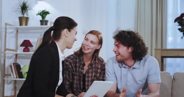 Portrait of attractive young couple chatting with their real estate agent on the sofa they have a discussing about house plan while using a tablet — Stock Video