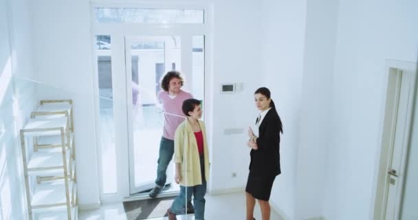 Impresionante casa luminosa de la mujer de entrada agente de bienes raíces que muestra la casa a su cliente casado pareja joven muy emocionados que buscan el interior de la casa — Vídeo de stock