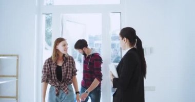 Güneşli bir gün çekici kadın ajan evde yeni bir karizmatik çift için modern evi temsil eden çok ev tasarım ajan womna ev göstermek için elleri ile gesticulating etkilendim