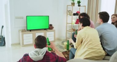 Çok etnik arkadaş heyecanlı grup yeşil bir ekran ile tv'de bir futbol maçı izlerken onlar mutlu destek ve takımlarının ilk hedefi kutluyor , bağırarak ayağa kalkarak ve ellerini yukarı olsun