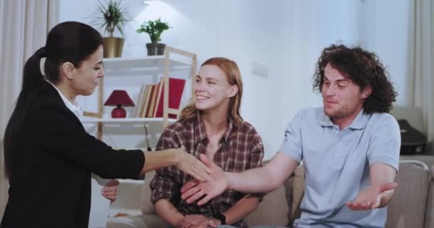 Closeup egy nappaliban karizmatikus pár, hogy foglalkozik a ház ügynök bérelni egy házat, hogy kezet rázott az ingatlanügynök és boldog pár átölelve egymást — Stock videók