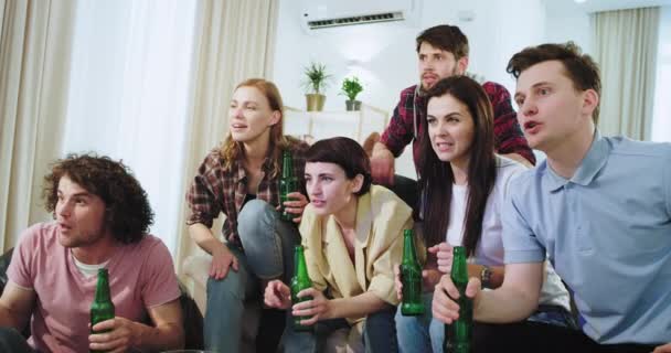 Konzentrierte und aufgeregte Freunde feiern glücklich das erste Tor ihrer besten Fußballmannschaft vor dem Fernseher, klatschen in die Hände und jubeln mit Bierflaschen — Stockvideo