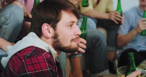 Nahaufnahme einer Gruppe multiethnischer Freunde, die konzentriert und aufgeregt ein Fußballspiel vor dem Fernseher im Wohnzimmer verfolgen, Bier trinken und ein paar Snacks essen — Stockvideo