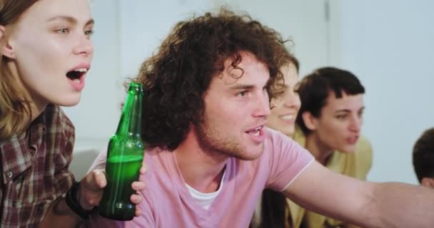 Portrait of charismatic young group of friends in front of TV support their best football team very emotional they are excited how the team play yelling and cheers with beer bottles in a very friendly — Stock Video