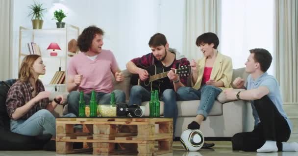 Amigos muy atractivos y artísticos multi étnicos disfrutan del tiempo juntos mientras cantan en una guitarra pasan un buen rato en la sala de estar tienen una fiesta chill — Vídeo de stock