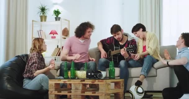 En una casa moderna grupo de gente bonita se divierten juntos cantando en una guitarra y bailando en una amplia sala de estar disfrutando del tiempo — Vídeos de Stock