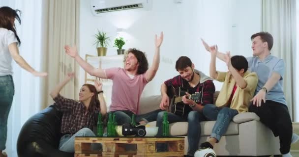 In einem modernen Haus in einer großen Firma haben Freunde Spaß zusammen auf einer Gitarre zu spielen, Bier zu trinken und die gute Zeit zu genießen — Stockvideo