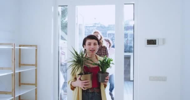 Рухаючись день для пари молодих подруг увійти в будинок вона була вражена дизайном будинку, тримаючи два квіти, пара і друг входять ззаду, тримаючи великі коробки — стокове відео