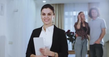 Karizmatik ve güzel bir ev ajanı kamera portre önünde onlar var yeni bir evin tadını geri genç çift ise kameraya doğru bakıyor