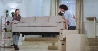 Çekici genç çift için hareketli gün onlar geniş bir oturma odasının ortasında kanepe taşıyan mutlu onlar yeni bir evde birlikte an zevk