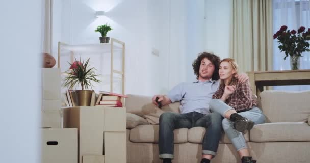 Di depan TV di sofa pasangan karismatik menikmati waktu di sebuah apartemen rumah baru mereka senang berdiri dari sofa dan keluar dari kamera — Stok Video