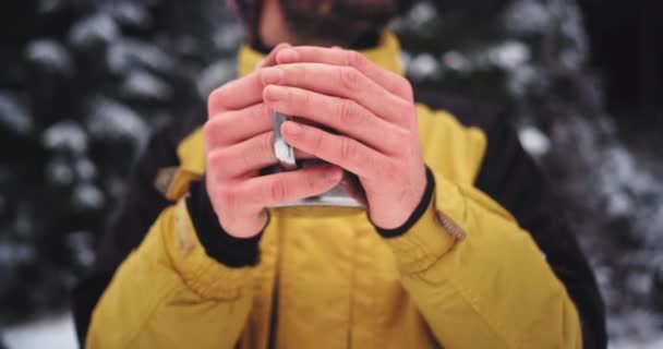 Détails gros plan des mains congelées d'un touriste au milieu de la forêt enneigée boire un peu de thé de tasse de fer — Video