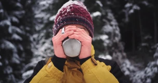 山の真ん中で鉄のコップからお茶を飲むかわいい顔をした若い観光客の肖像画、彼は手を凍らせた — ストック動画