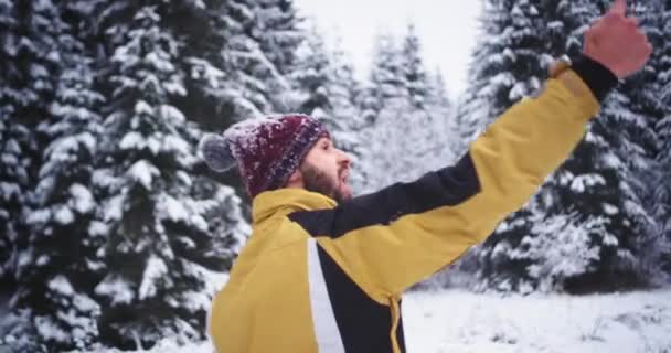 カリスマ的で格好良い観光客は、冬の日に雪の森の真ん中に自分の携帯電話で自分撮りを取る、彼はこの素晴らしい場所を設立したことを非常に幸せに — ストック動画