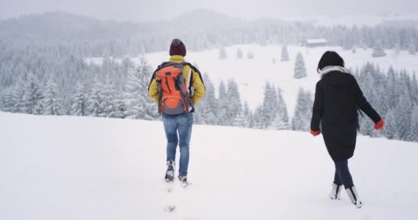 Egy téli napon két turista férfi és nő séta a havas területen, fagyasztott mennek a rendeltetési helyükre, csodálatos táj körül — Stock videók