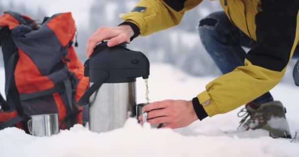 Detalhes de close-up no meio do turista de inverno obter alguma bebida quente de sua garrafa térmica em uma xícara de ferro no meio do campo nevado — Vídeo de Stock