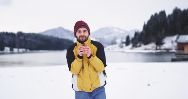 Primer plano muy feliz y carismático joven turista bebiendo de la taza de hierro un poco de té en medio de un paisaje increíble con un lago y una montaña gesticulando con las manos y mostrando a la cámara — Vídeos de Stock