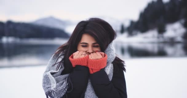 Mulher bonita ficando congelante fora no meio do dia de inverno, close-up da câmera ela está muito feliz, fundo incrível vista do lago e neve montanha e floresta — Vídeo de Stock
