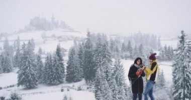 Genç ve çekici bir adam ve bayan arka planda dikiliyorlar. İnanılmaz karlı bir orman. Daha önce çektikleri fotoğraflara bakıyorlar.
