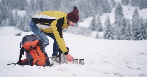 Турист путешествует один в зимний день, он прибыл в красивое место с удивительным ландшафтом, он взял свою оранжевую сумку и держа железную чашку с горячим чаем — стоковое видео