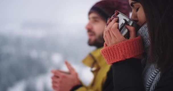 Detaljer porträtt av två unga turist dricka lite hett te, i fantastisk vinterplats i toppen av berget med snöiga skog — Stockvideo