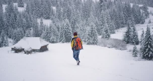 Caminante turista equipado a través de la nieve a la increíble casa de madera en el campo en medio de la montaña y el bosque — Vídeos de Stock