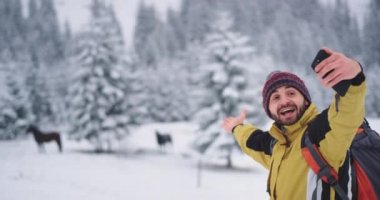 Dağ ve karlı ormanın ortasında atlarla selfie çeken gülümseyen turist, akıllı telefonuyla fotoğraf çektirmekten çok mutlu