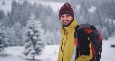 O dağda seyahat kamera önünde gülümseyen büyük mutlu turist adam , karlı orman etrafında kışın şaşırtıcı manzara