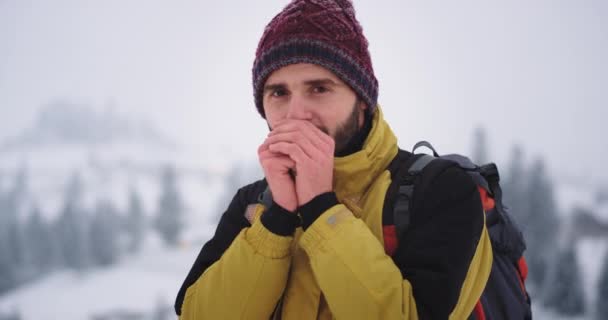 Karismatisk ung turist porträtt lycklig resa i mitten av berget han ser till kameran har röda kalla händer han visar landskapet och fantastisk utsikt runt honom till kameran — Stockvideo