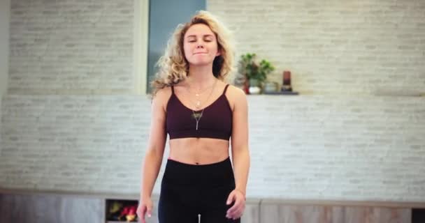 Mujer rubia carismática agitando la cabeza delante de la cámara con una ropa deportiva lista para comenzar un ejercicio aeróbico en un estudio de yoga wellness — Vídeo de stock