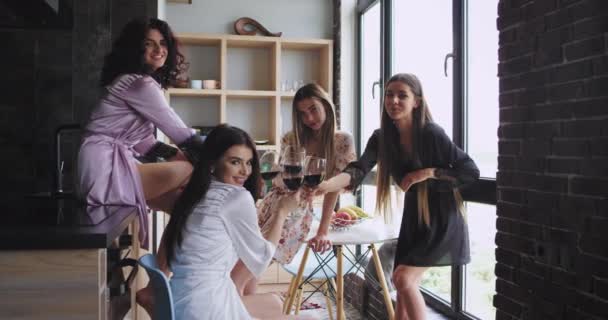 Группа из четырех дам проводит время вместе, выпивая вино в пижаме дома, в доме в городском стиле с панорамным видом — стоковое видео