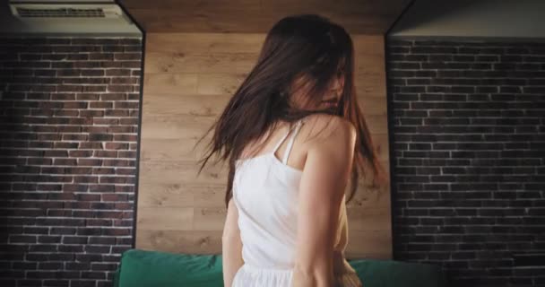Brünette Dame mit langem Haar springt und tanzt im Pyjama vor der Kamera sehr sinnlich und genießt die Zeit — Stockvideo