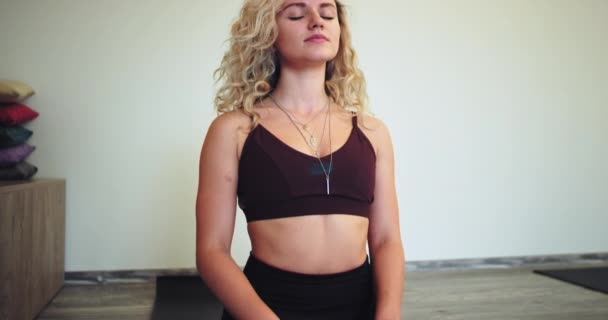 Részletek rögzítése egy karizmatikus nő nyugodt és koncentrált ő áll a jóga meditációs idő ülve a padlón egy jóga stúdióban van egy jó hangulat, és mosolygó arcok — Stock videók