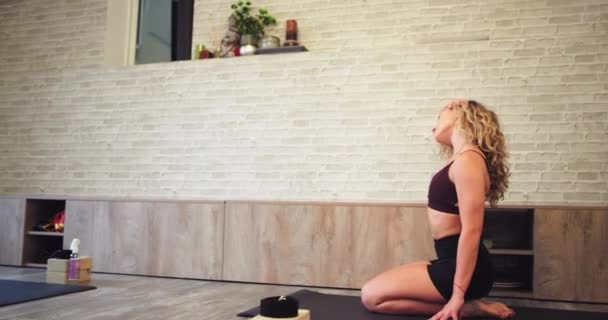 Lady i en sportkläder på sport mattan öva stretching kroppsövningar på yogastudion hon känner sig avslappnad och koncentrerad har en hälsosam livsstil — Stockvideo