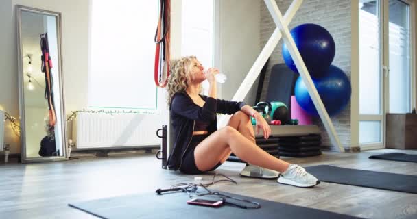 Lady po ciężkim treningu uczucie zmęczenia ma relaksujący czas picia wody w studiu aerobik, ona ubrana w specjalnej odzieży sportowej — Wideo stockowe