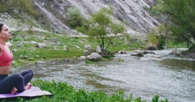 Taşlar ve nehir genç bayan o bir meditasyon pozlar var mat yoga ile inanılmaz manzara ortasında , o özel yoga giysileri giyiyor