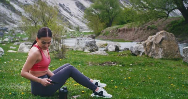 Szomjas hölgy után kemény edzés ivott egy kis vizet tőle sport palackot, és élvezi a kilátás a természet közepén egy nagy kövek és a friss levegő — Stock videók