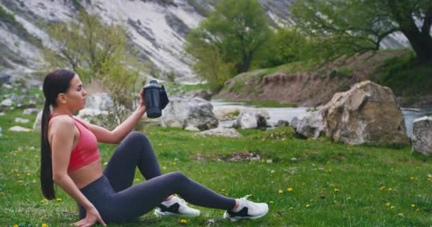 Charyzmatyczny z doskonałą Lady ciała po ciężkim treningu na łonie natury, idąc przez trawę siedzi w dół i korzystających z ciszy spragniony pić trochę wody i uczucie szczęśliwy — Wideo stockowe