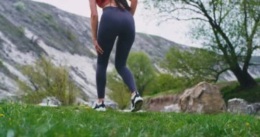 Şaşırtıcı manzara ortasında sportif bir bayan ayrıntıları arkadan video alarak çalıştırmak için hazır olsun , yeşil alan büyük kayalar etrafında