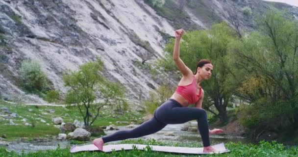 Sportos hölgy visel kényelmes sportruházat és gyakorló jóga lány stretching az egész testet a szőnyegen a természet közepén — Stock videók
