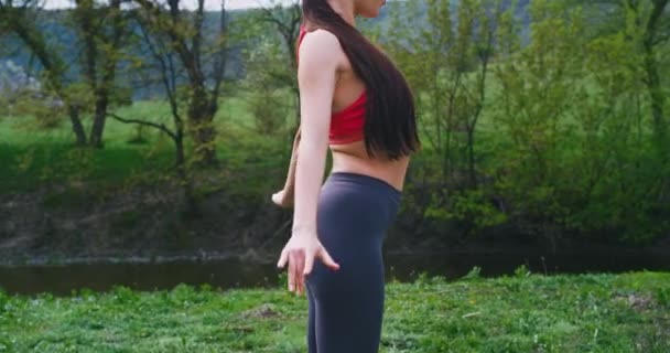 Привлекательная женщина в спортивной одежде посреди природы она растягивает тело перед камерой очень сосредоточенно она делает свои тренировки на свежем воздухе — стоковое видео